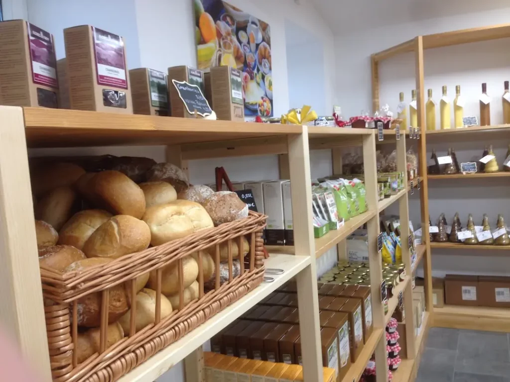 Ein geflochtener Weidenkorb voll frischer, goldbrauner Brötchen auf einem Holzregal im Hofladen Geflügelhof Arnsdorf.