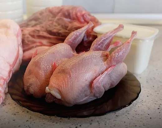 Küchenfertig vorbereitetes Wachtelfleisch auf einem dunklen Glasteller in der Küche des Geflügelhofs Arnsdorf.