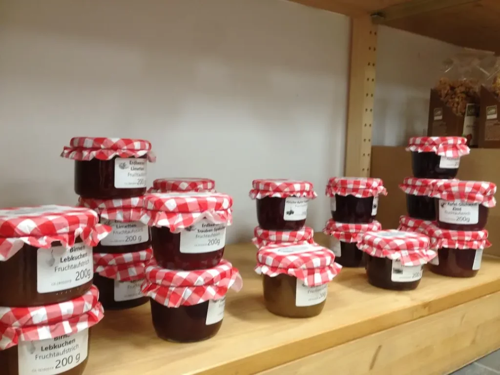 Gläser mit Fruchtaufstrichen wie Birne-Lebkuchen und Erdbeere-Limette mit rot-weiß karierten Stoffdeckeln im Verkaufsregal.